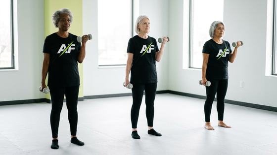 Three women over 60 doing controlled bicep curls with light dumbbells